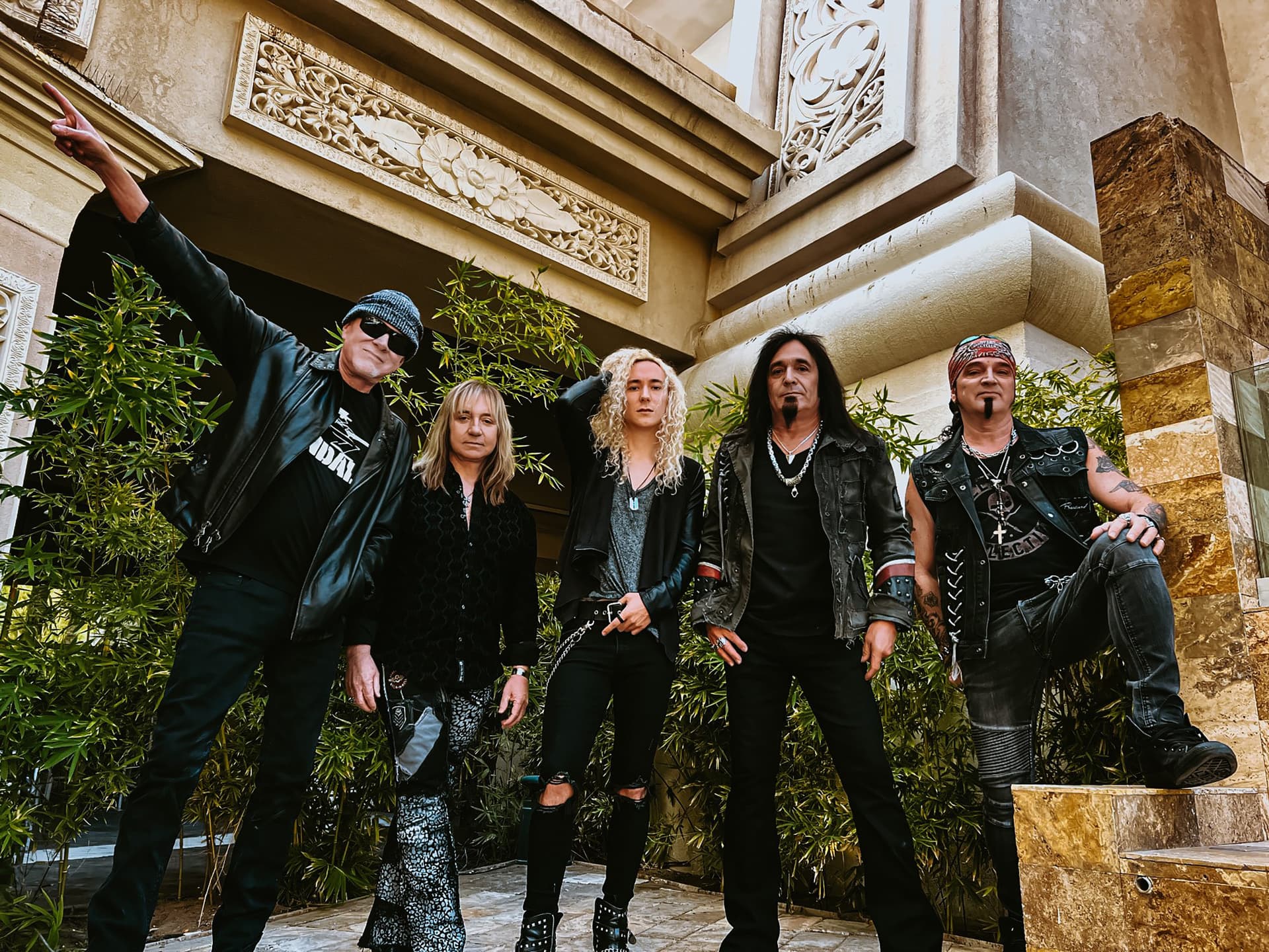 Great White band lineup in leather and denim posing in front of an ornate carved stone building