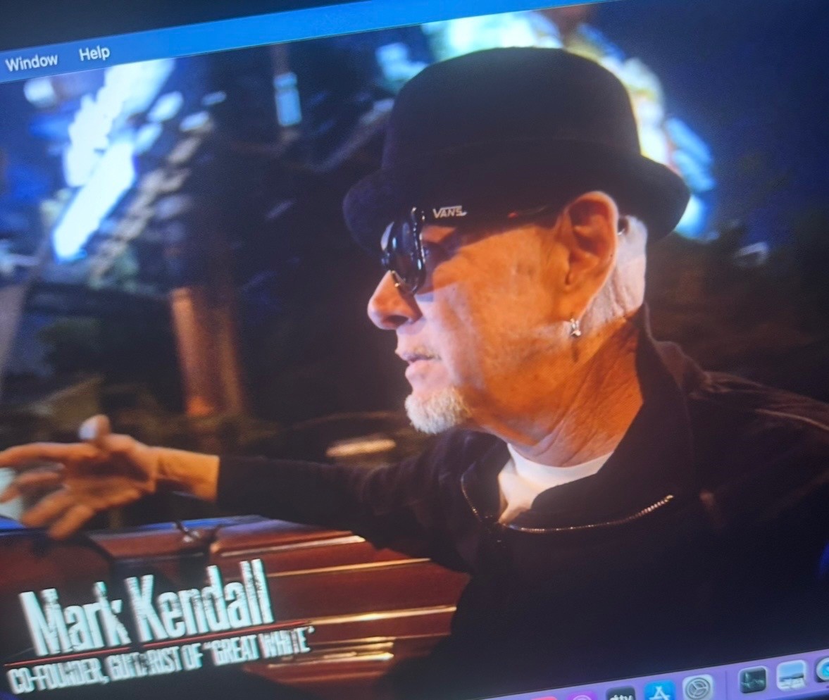 Profile shot of Mark Kendall in a bowler hat and sunglasses under blue stage light