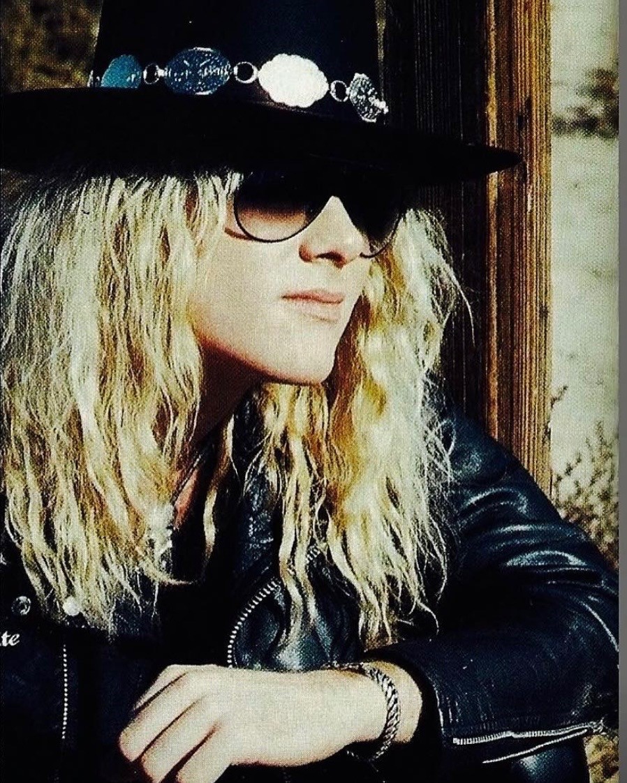 Young Mark Kendall in a jeweled hat and leather jacket outside a desert cabin