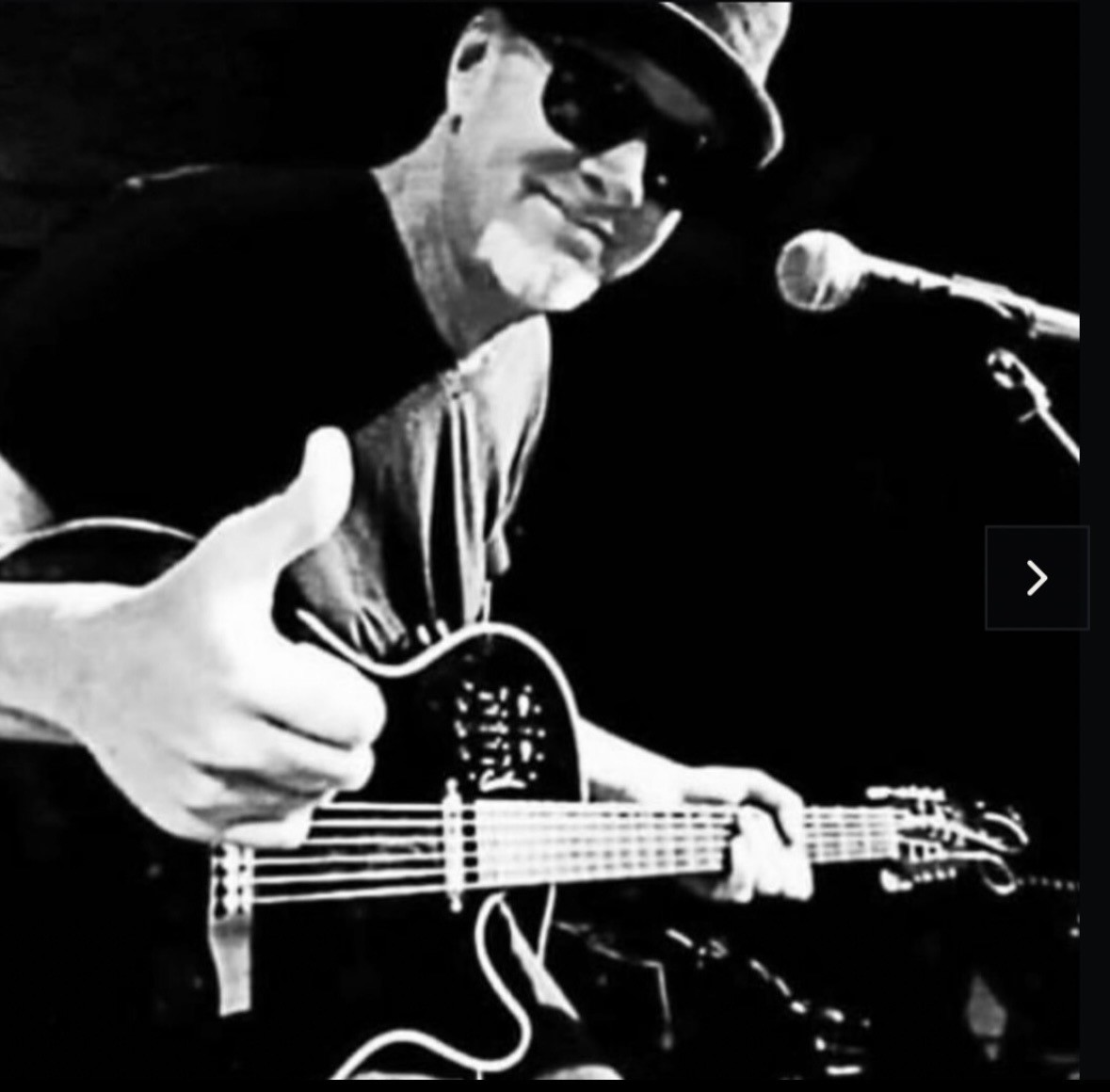 Mark Kendall playing a resonator guitar at the microphone in black and white