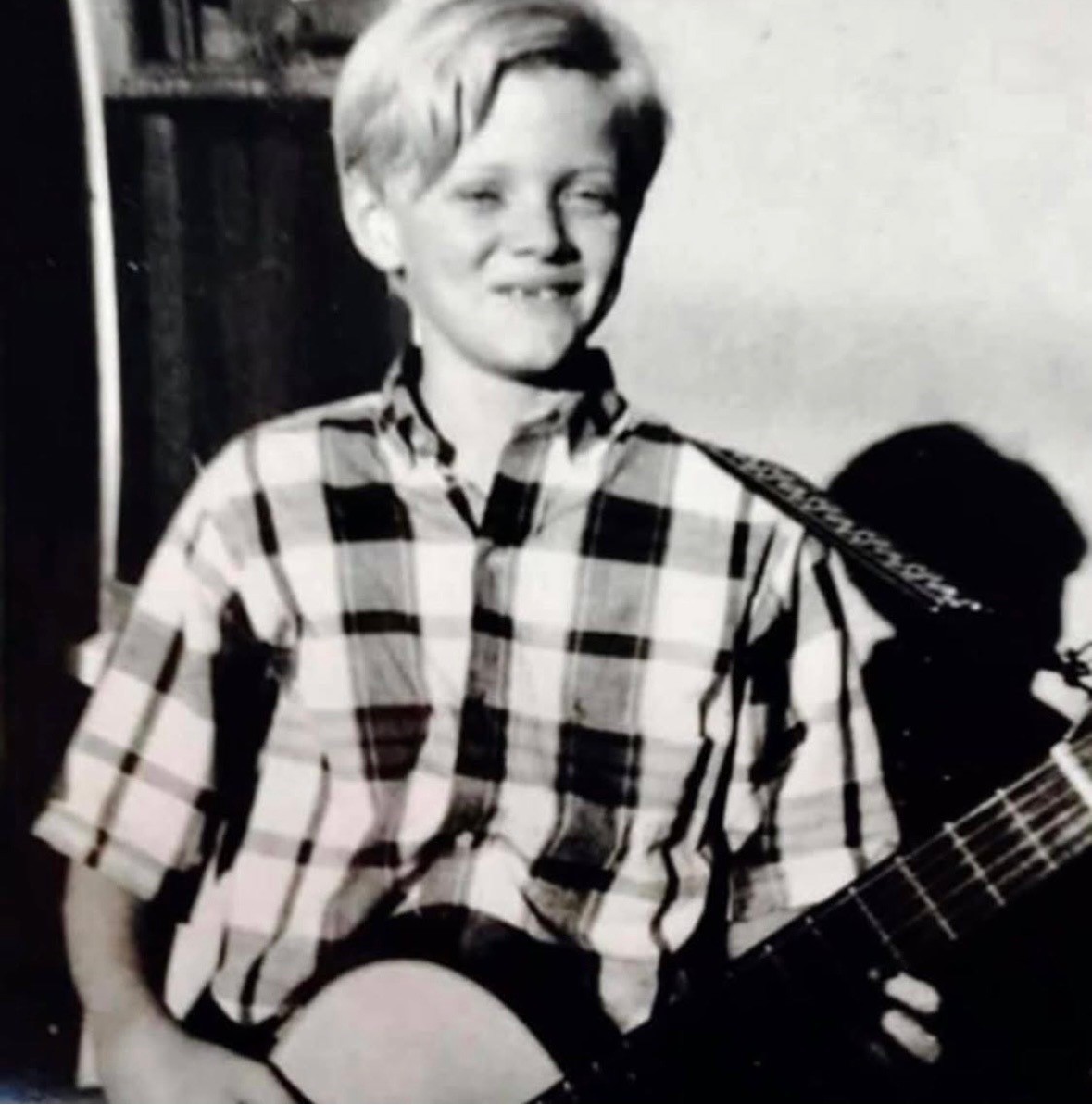 Young Mark Kendall smiling while holding an acoustic guitar