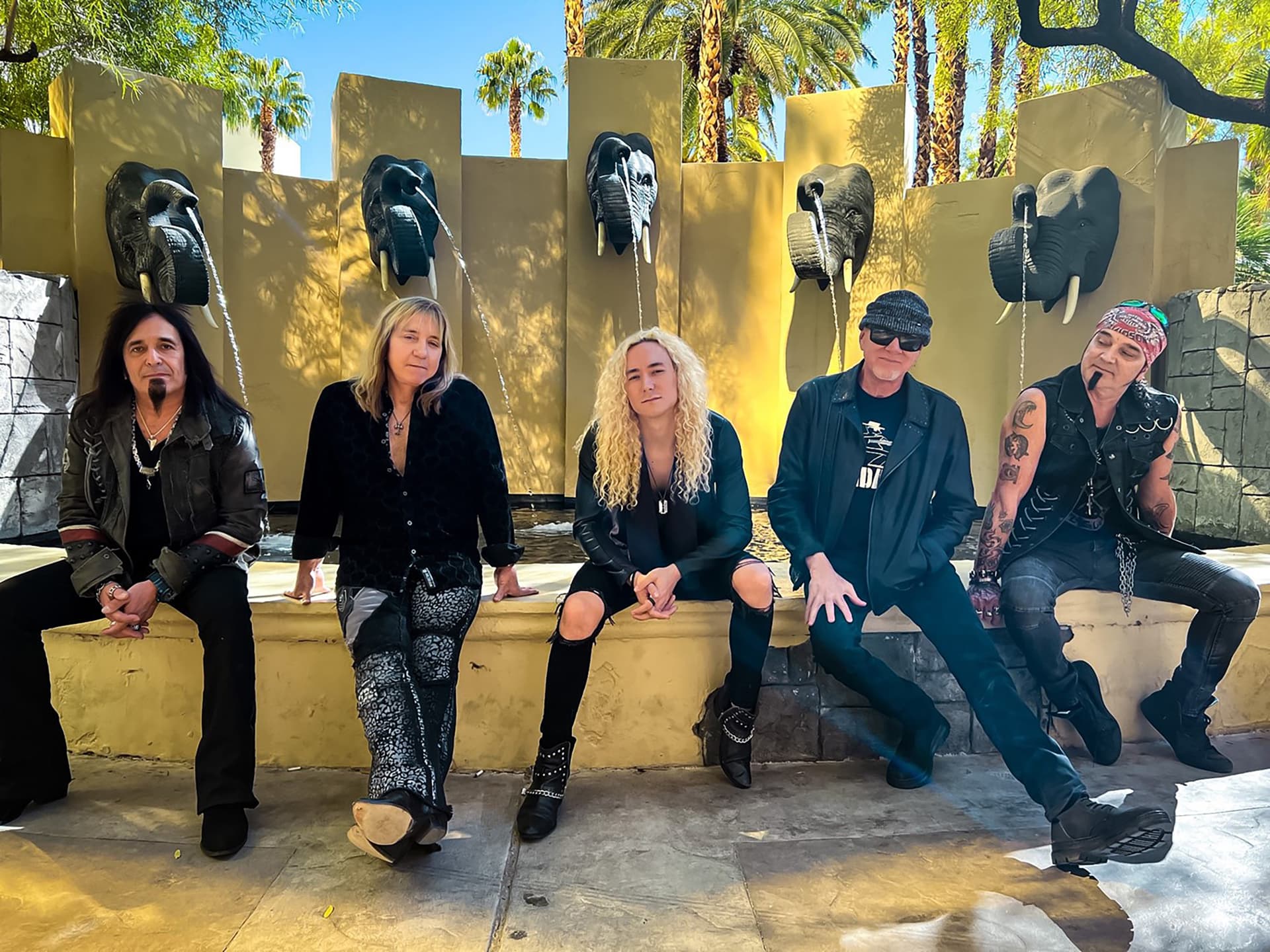 Great White band seated together by an elephant fountain in 2023